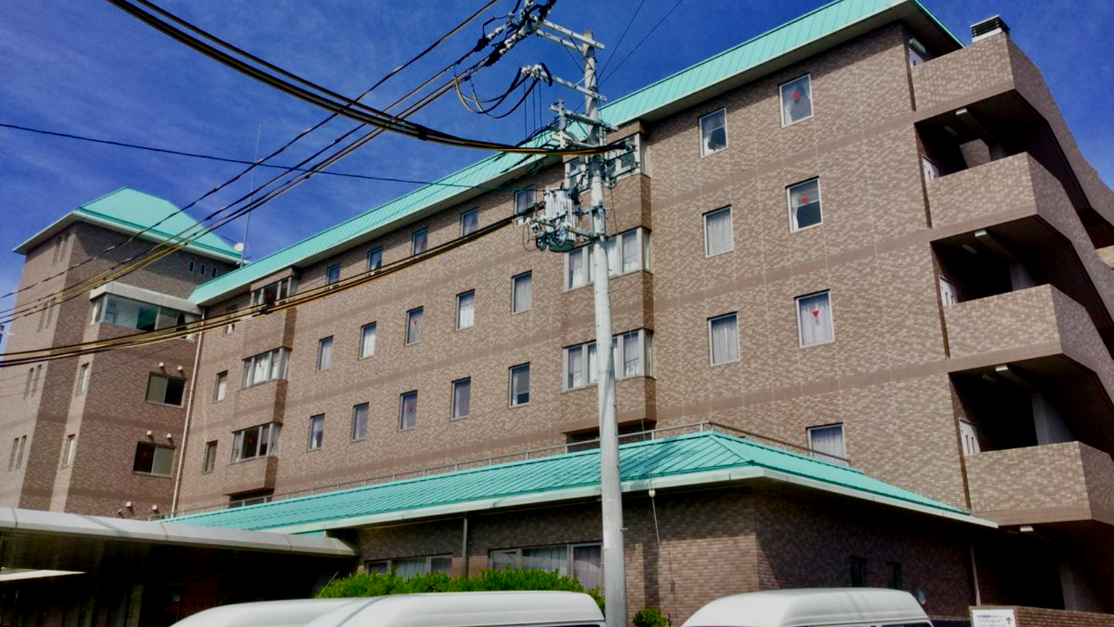 介護施設の建物外観。レンガ造りの4階建て建物で緑色の屋根が特徴。